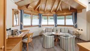 A cozy room with a wooden ceiling, a sofa set, a small table, and a window with curtains. - Hotel Flora (Livigno)