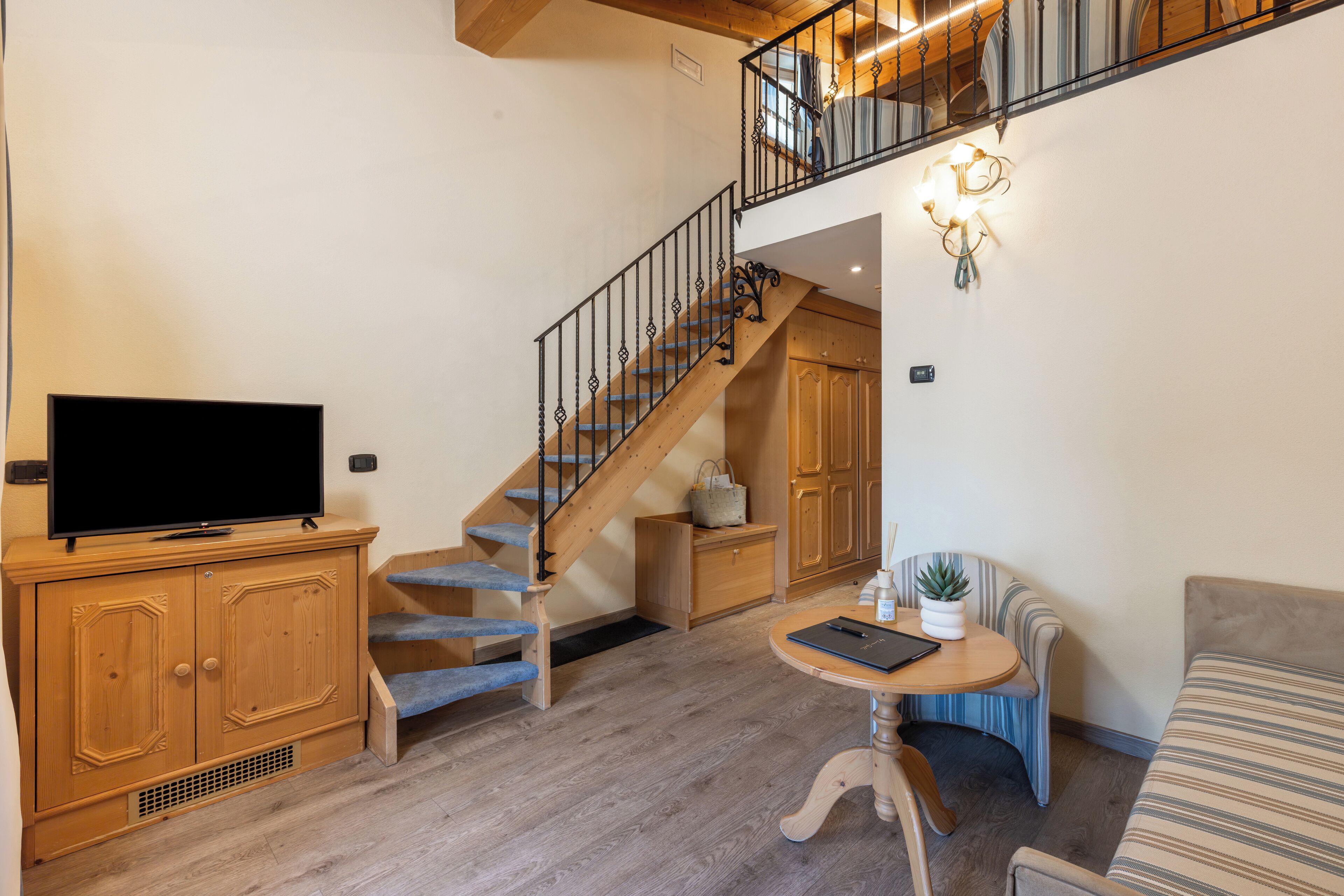 Una sala de estar con televisión, escalera de madera, una mesa de comedor y un sofá.