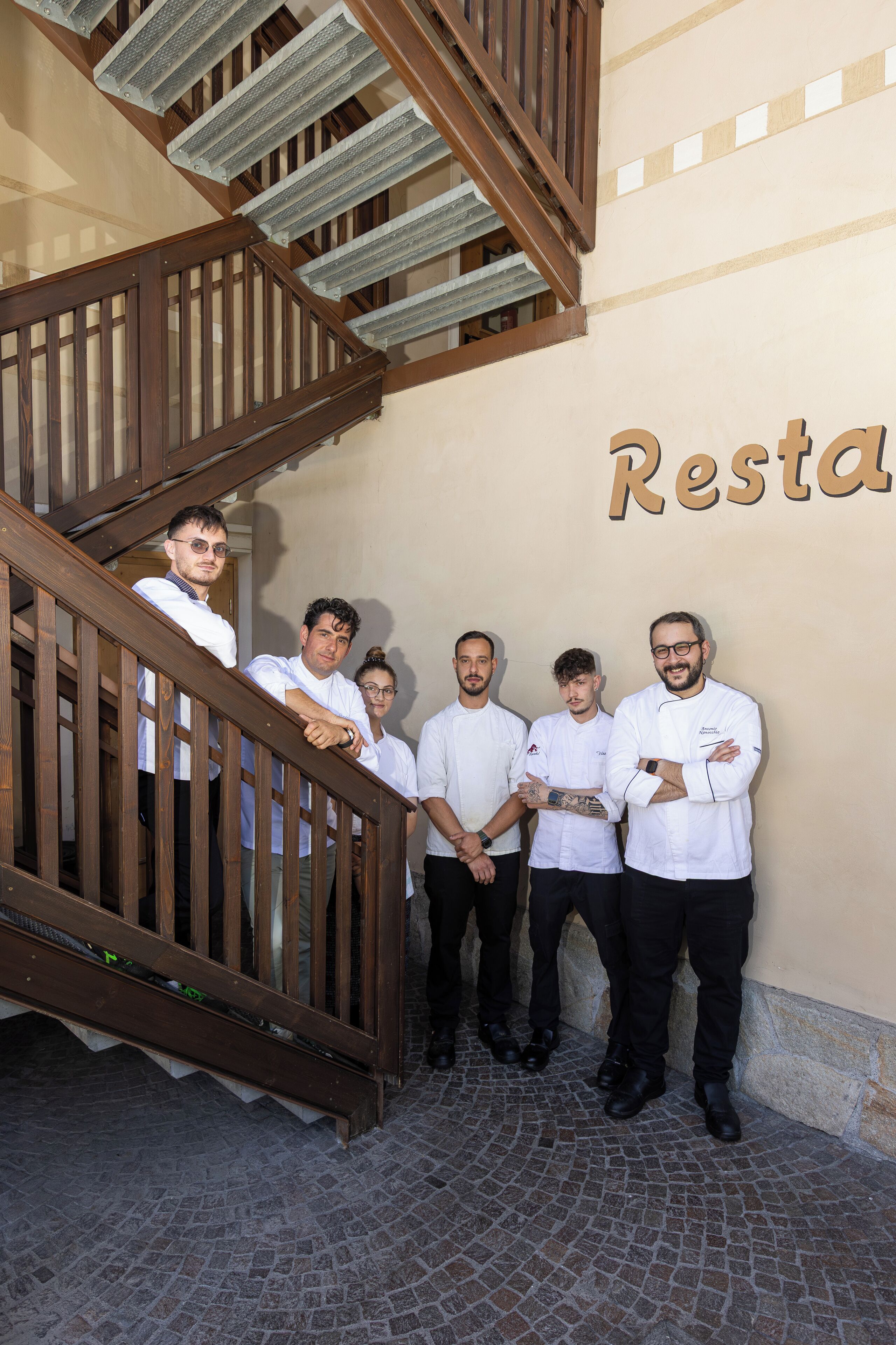 A group of people standing on a cobblestone floor with a staircase and a wall with the word 'Resta' partially visible.