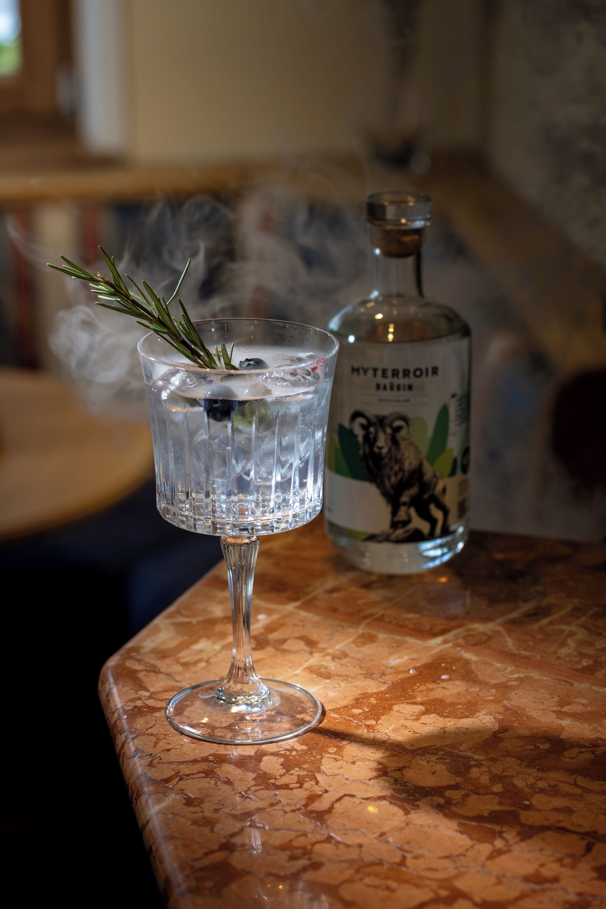 Ein Glas mit Rosmarinzweig und eine Flasche mit dem Aufdruck "HYTERROIR" auf einer Marmorarbeitsplatte.