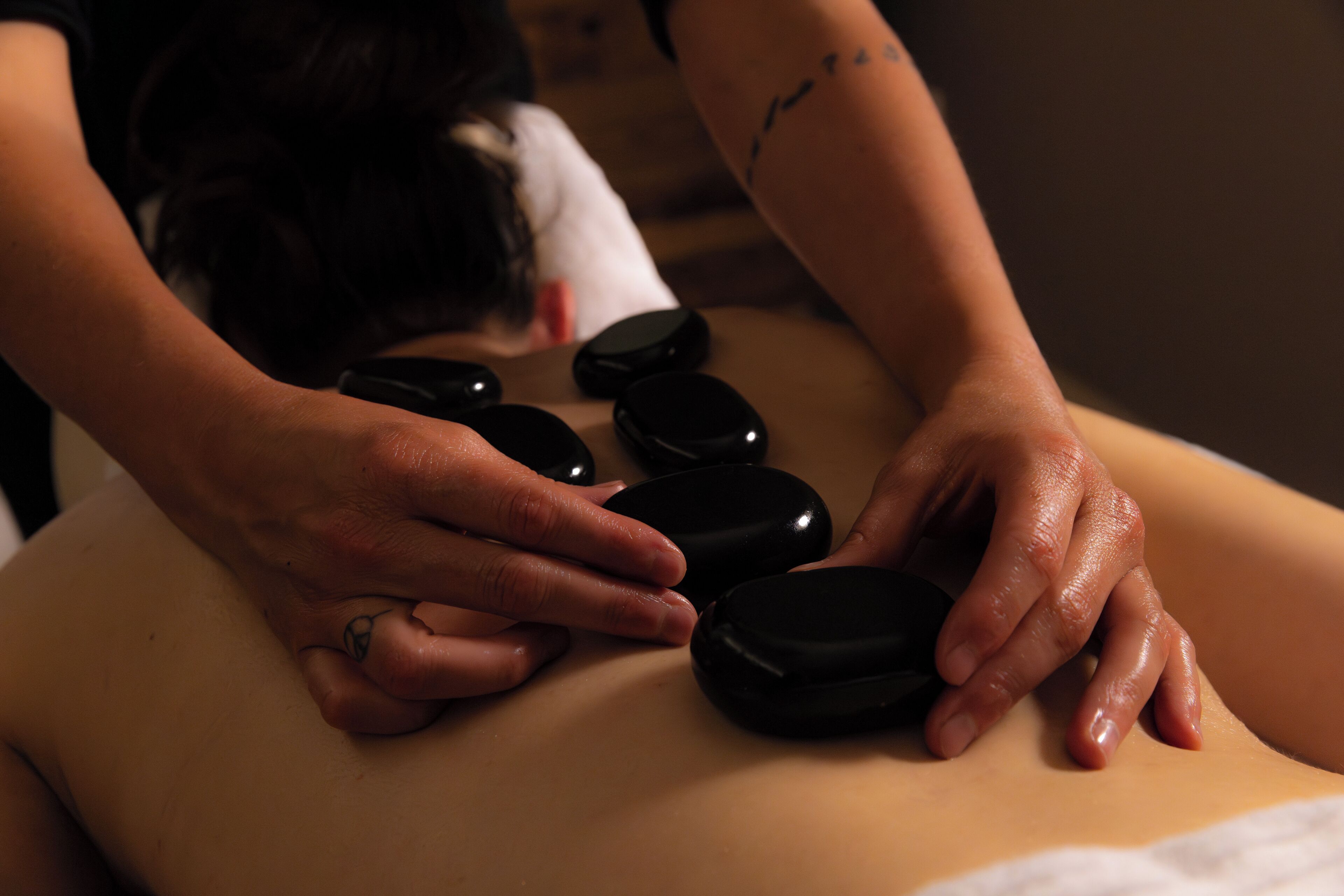 A massage therapy session with a person receiving a back massage using black stones.