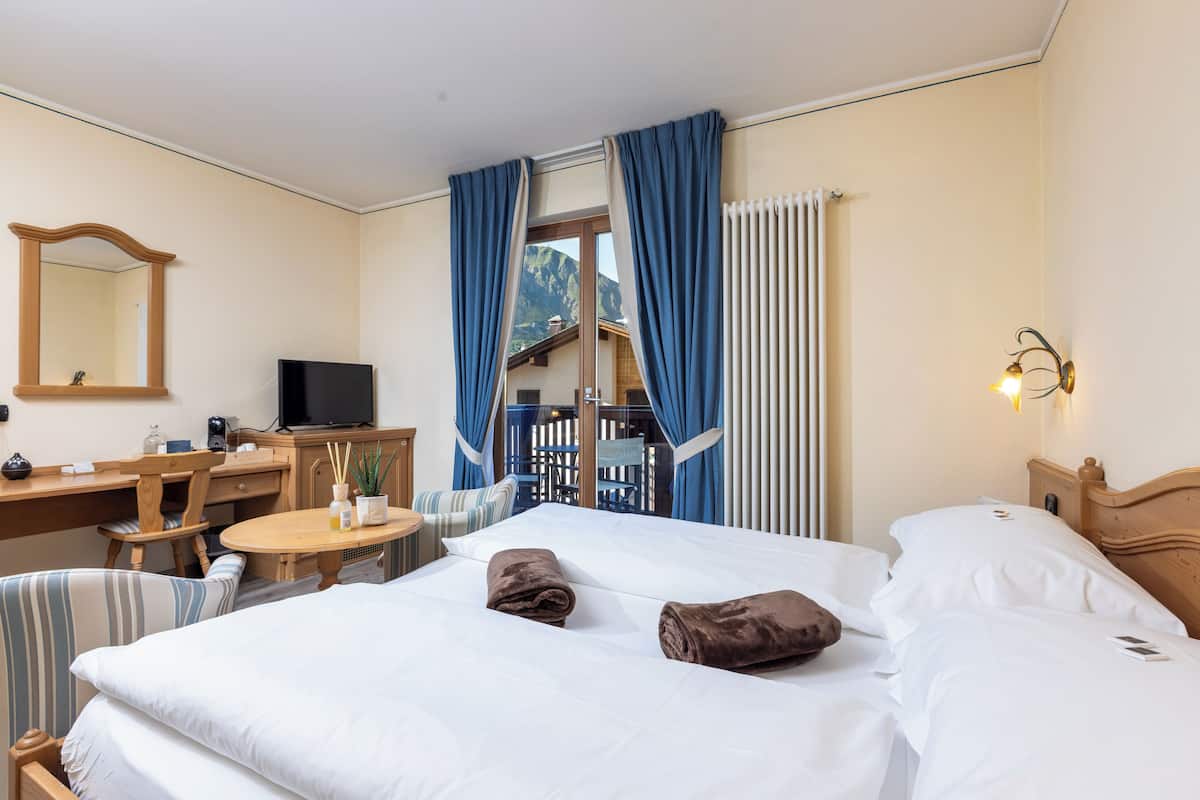 A hotel room with a bed, a desk, a chair, a table, a TV, and a view of the mountains.