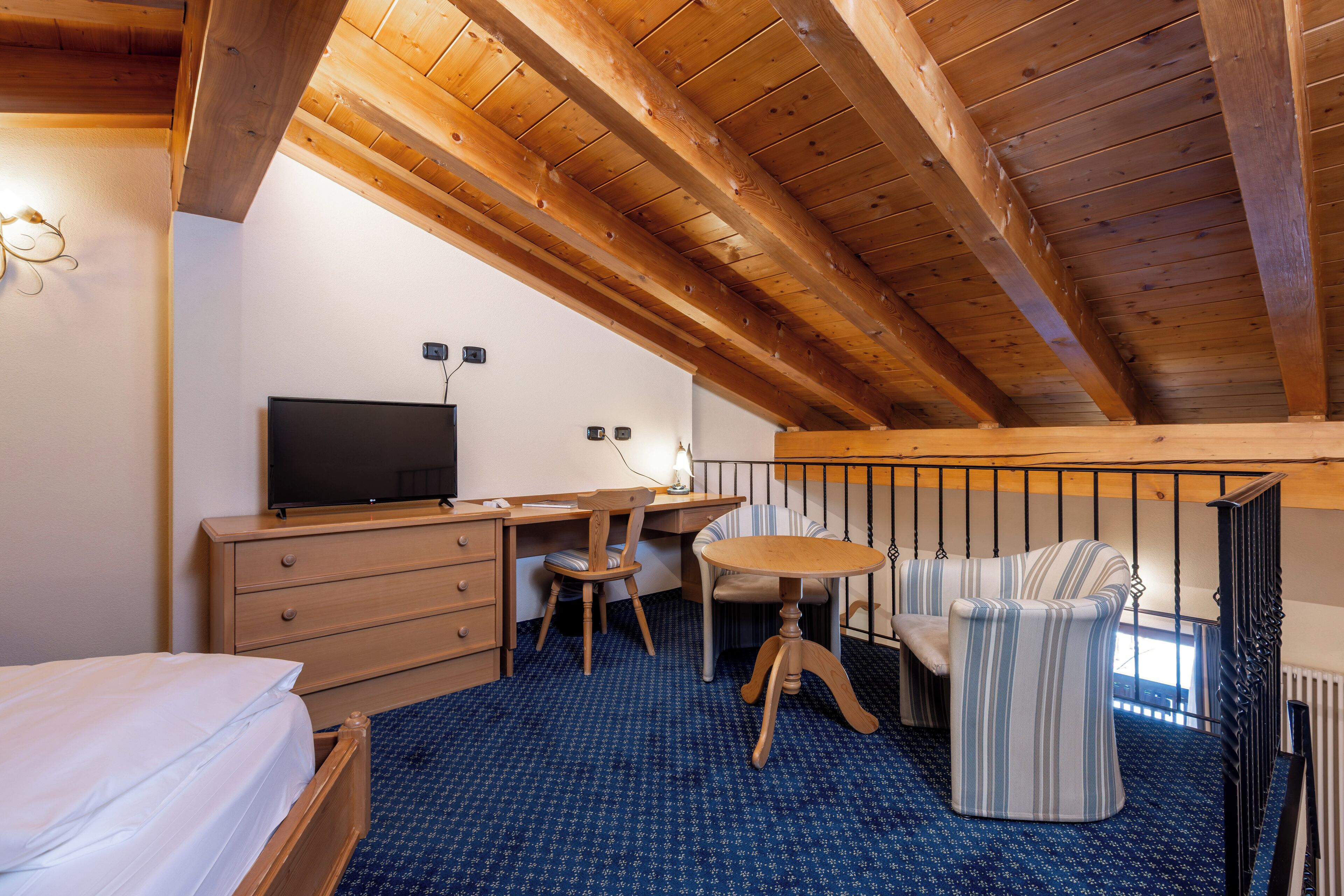 Une chambre avec un lit, un bureau avec une télévision, une chaise, une petite table et une fenêtre donnant sur un beau paysage.