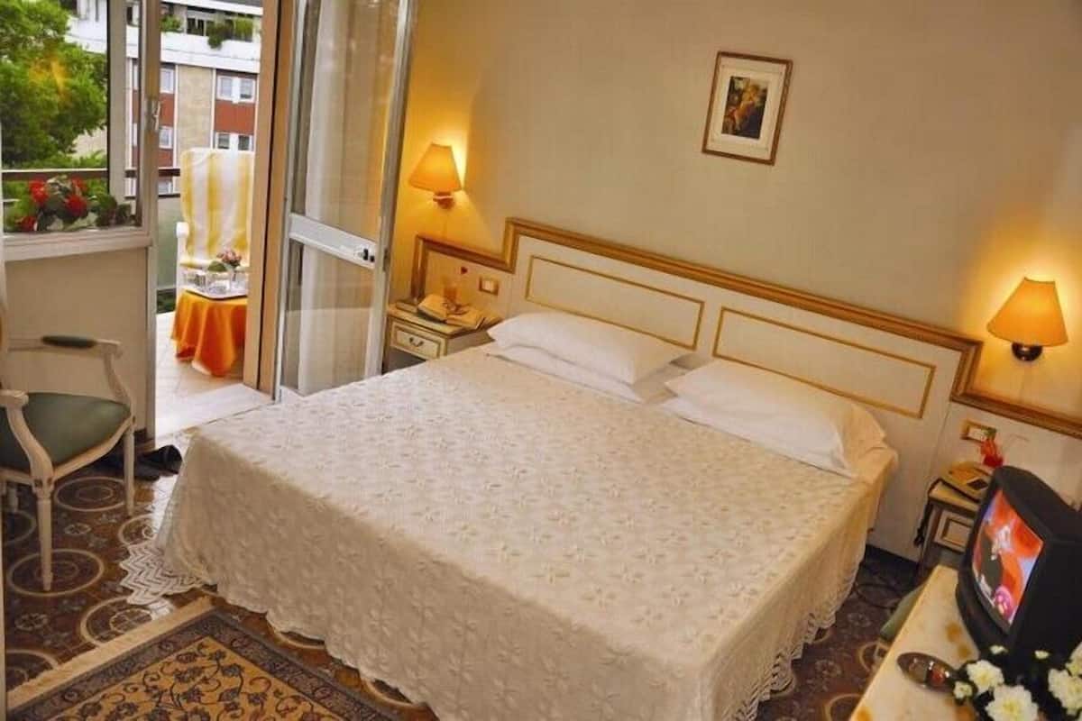 Une chambre d’hôtel avec un grand lit, deux lampes de chevet, une télévision et une fenêtre donnant sur l’extérieur.