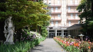 A building with a central entrance, surrounded by a garden with various plants and flowers. - Hotel Terme Villa Piave (Abano Terme)