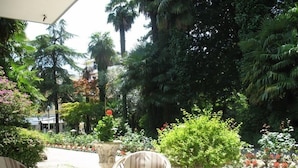 An outdoor seating area with wicker chairs and a yellow table, surrounded by lush greenery and flowering plants. - Hotel Terme Villa Piave (Abano Terme)