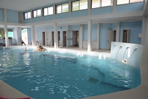 An indoor swimming pool with clear water, white walls, and multiple windows.
