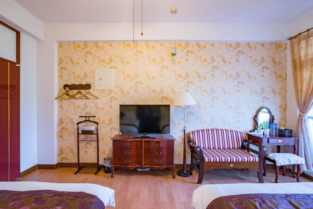 A hotel room with two beds, a TV, a dresser, a chair, and a desk.