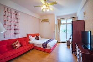 Quarto com cama, sofá vermelho, televisão e ventoinha no teto.