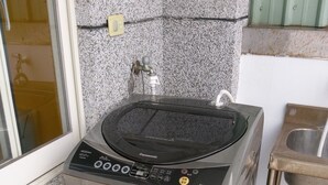 A compact, stainless steel washing machine with a control panel, located in a corner of a room with a granite countertop and a small sink. - Hualien Tour B&B (Xincheng)