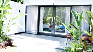 A modern room with a large sliding glass door leading to a balcony, a wooden chair, and potted plants. - Palm Garden Bali (Nusa Dua)