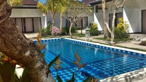 A swimming pool with a checkered pattern, surrounded by palm trees and a modern building with large windows. - Palm Garden Bali (Nusa Dua)