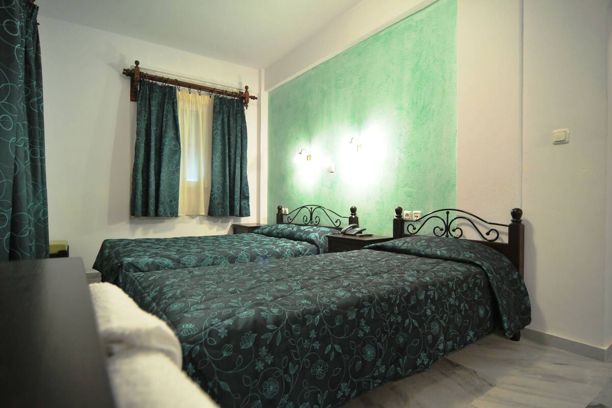 Un dormitorio con dos camas, una mesita de noche, una mesa y una ventana con cortinas.