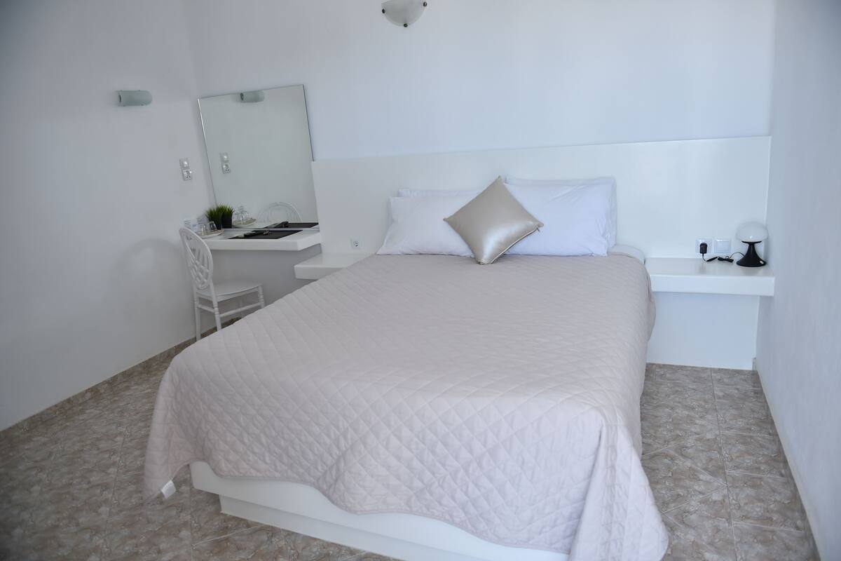 Un dormitorio ordenado con cama, mesita de noche, escritorio y silla.