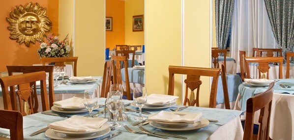 A dining area with tables set for four, wooden chairs, and a sun-shaped wall decoration. - Hotel Al Sole Terme (Abano Terme)