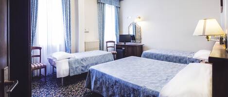 A hotel room with two beds, a desk with a computer, a chair, a lamp, and a window with curtains.