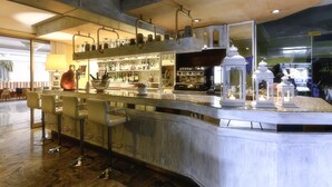 Een bar met een lange toonbank, diverse krukken en een ruime keuze aan flessen en glazen.