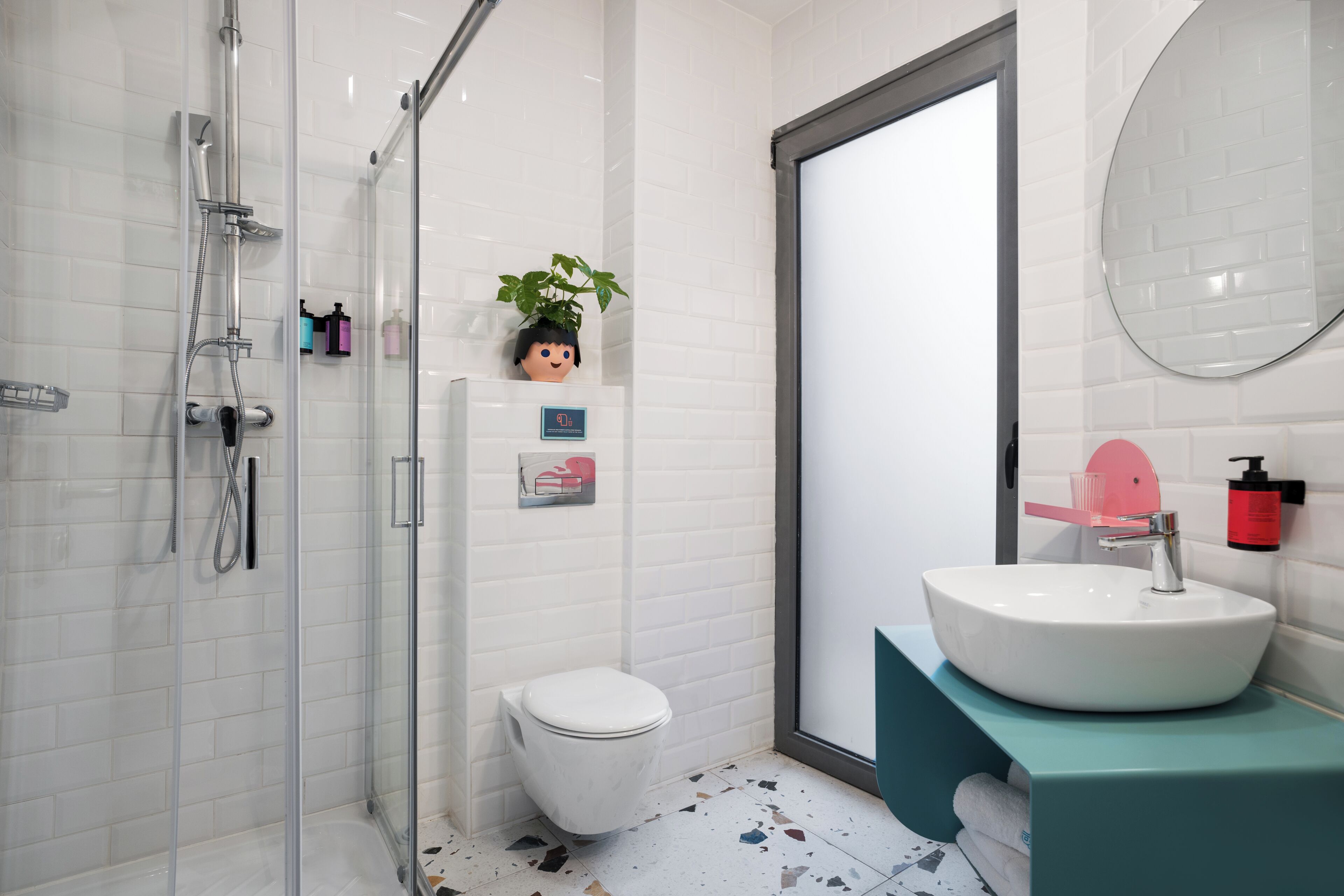 A modern bathroom with a glass-enclosed shower, a white toilet, a sink with a pink soap dispenser, and a mirror on the wall.