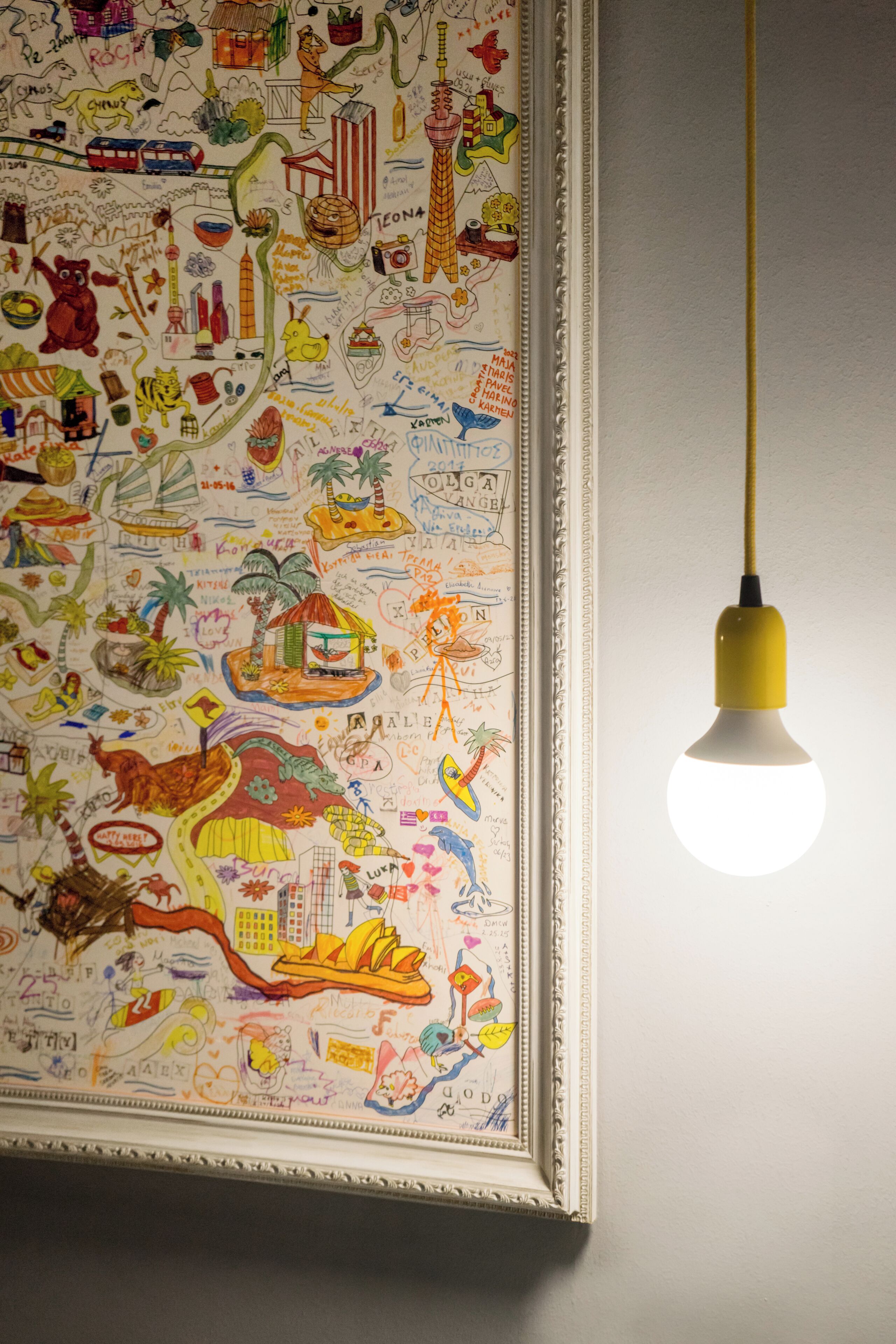 Un adorno de pared enmarcado con varias ilustraciones y texto, colgado en una pared con una lámpara colgante encima.