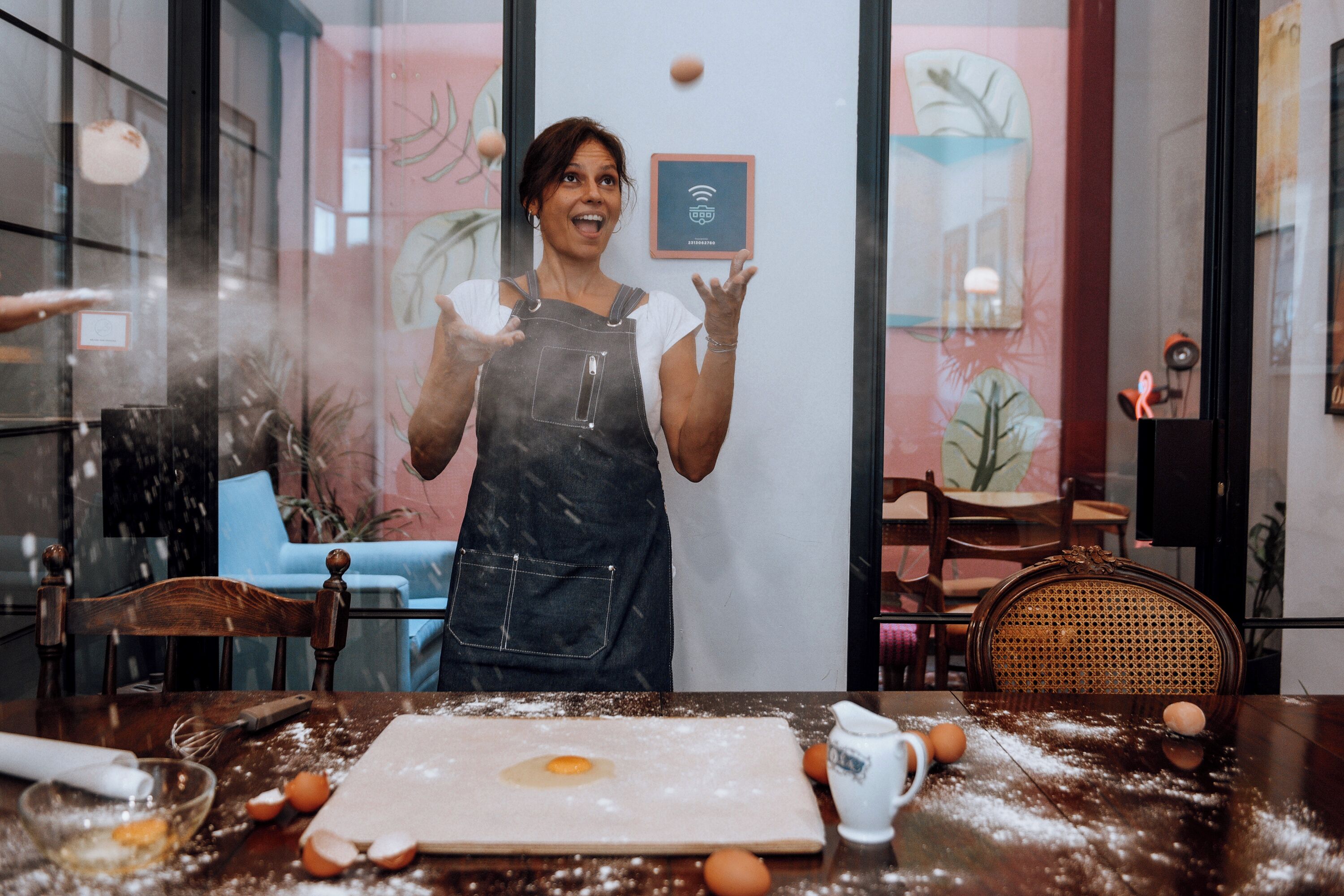 Una persona en una cocina con una mesa cubierta de harina, huevos y utensilios de cocina.
