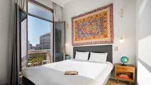 A hotel room with a large bed, a nightstand with a globe, and a view of the city through a balcony.
