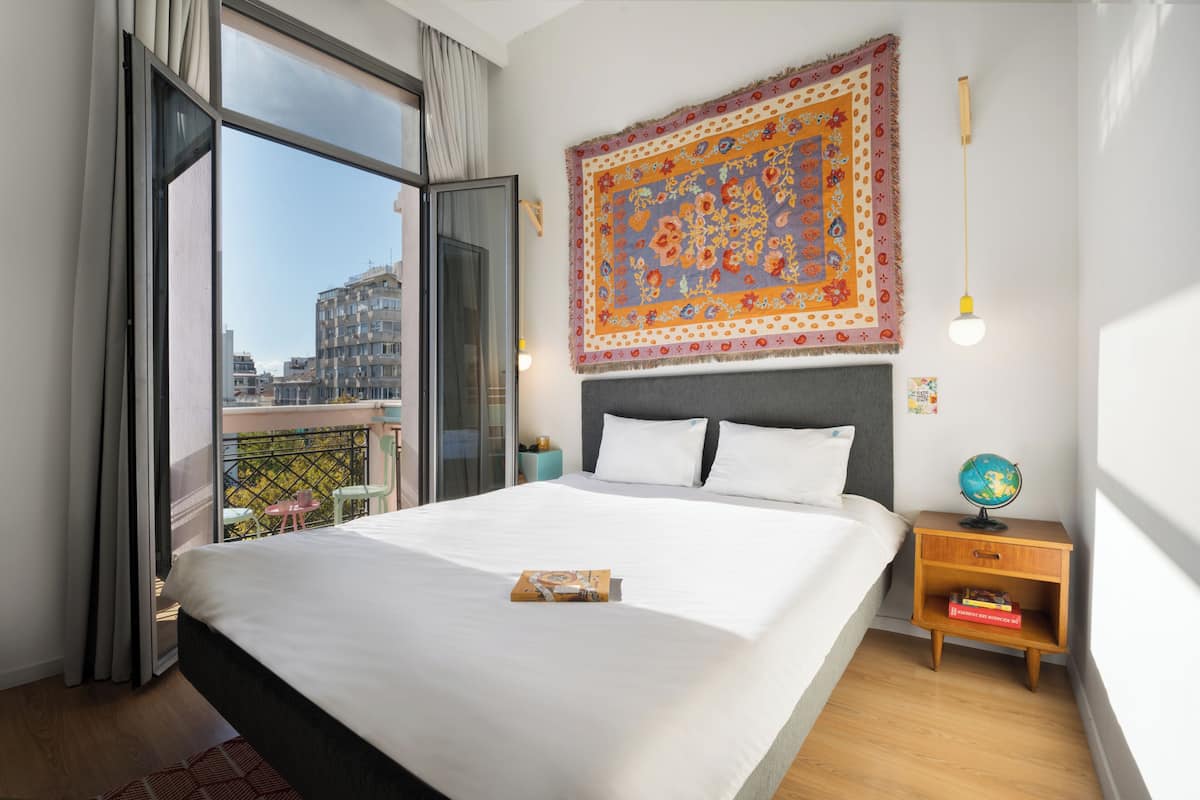 A hotel room with a large bed, a nightstand with a globe, and a view of the city through a balcony.