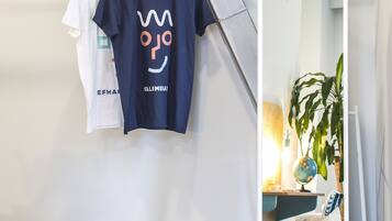 A room with a hanging rack holding two t-shirts, a mirror, a plant, and a chair.