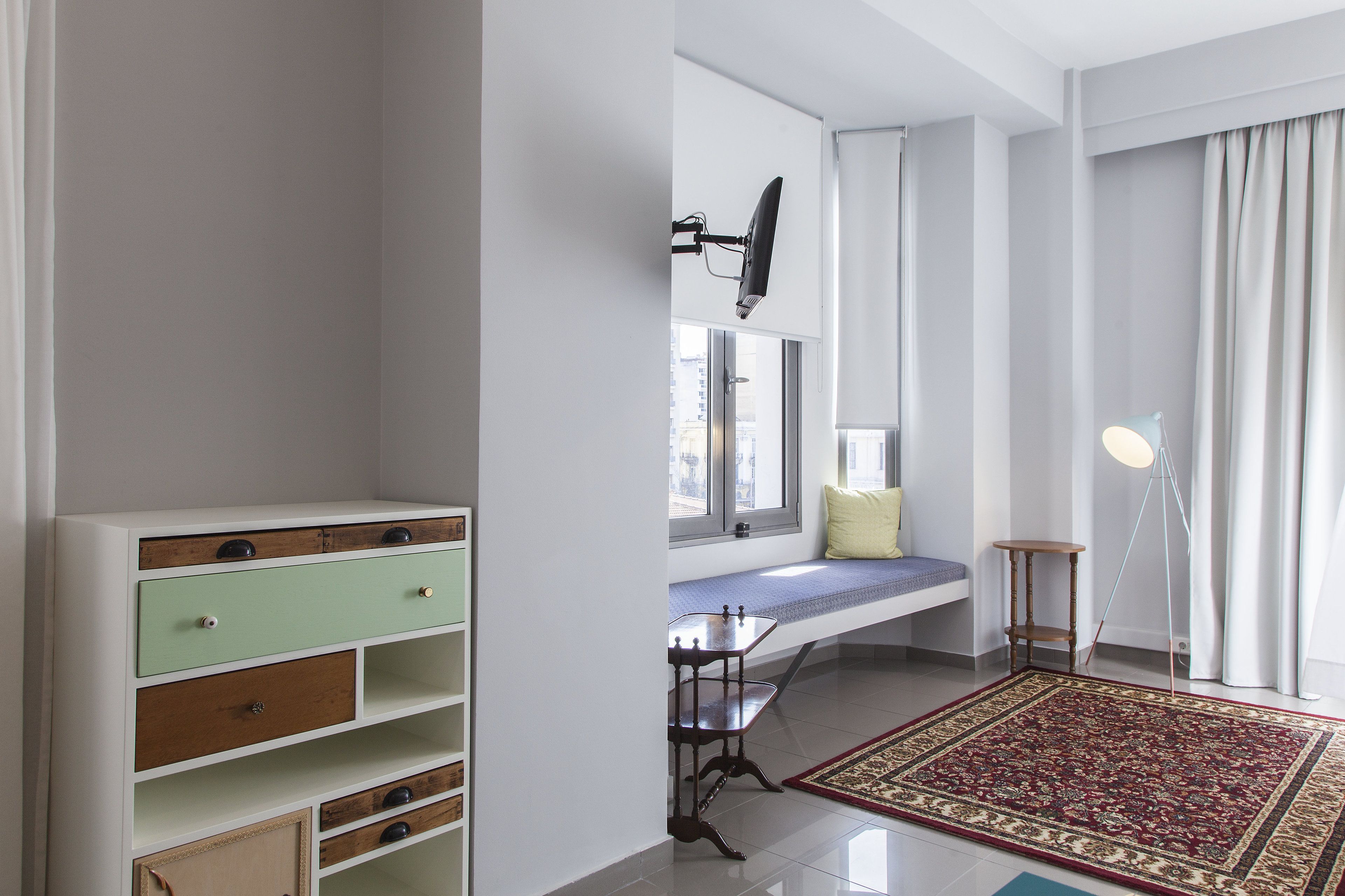 Ein Zimmer mit integriertem Sitzplatz, Schreibtisch, Lampe und großem Teppich.