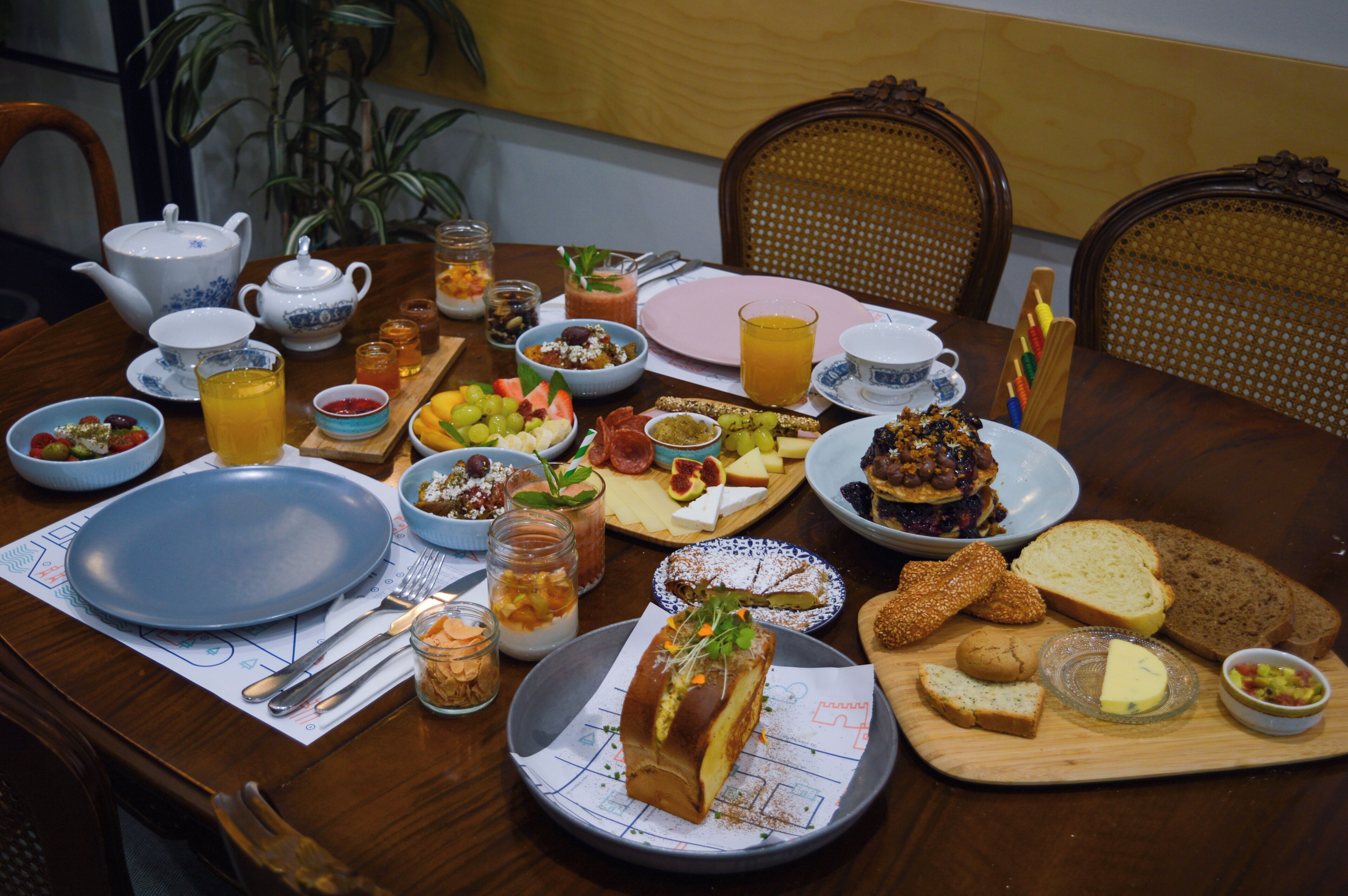 Mesa para desayunar dispuesta con diversos alimentos, frutas, pan y una bebida caliente.