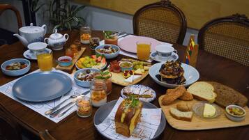Mesa para desayunar dispuesta con diversos alimentos, frutas, pan y una bebida caliente.