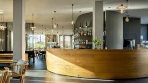 Un área de bar moderna con una barra curva de madera, luces colgantes y vistas al comedor al fondo.
