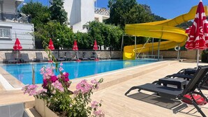 A swimming pool with a yellow slide, lounge chairs, and red umbrellas. - Park Avrupa Hotel (Kemer)