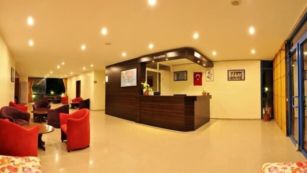 A hotel reception area with a curved reception desk, red upholstered chairs, and a flat-screen TV. - Park Avrupa Hotel (Kemer)