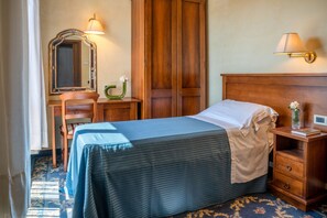 Quarto de hotel com cama, mesa de cabeceira de madeira, cômoda, espelho e abajur.