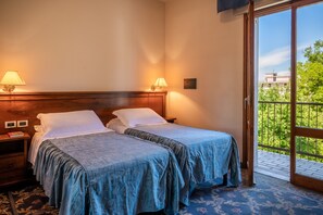 Quarto de hotel com duas camas, cabeceira de madeira, luminárias laterais, mesa de cabeceira e vista para área verde através de uma porta de vidro.