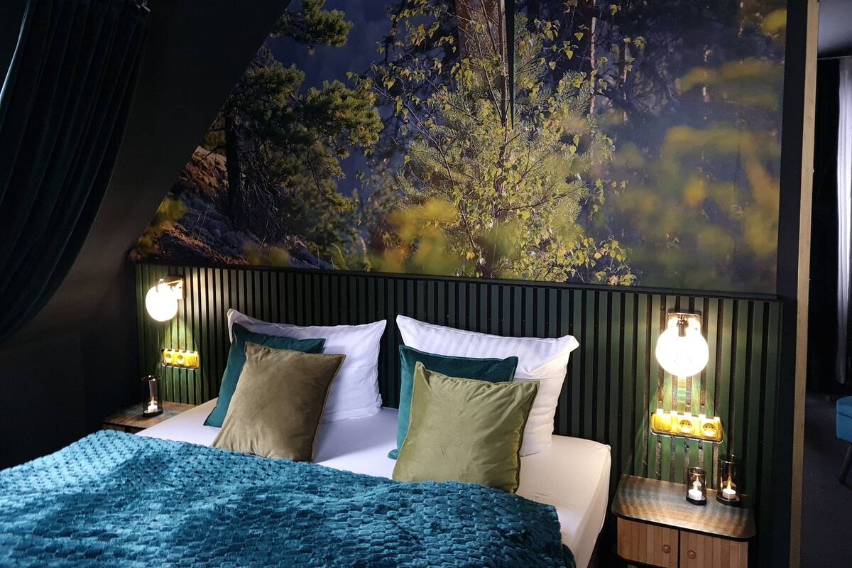 A bedroom with a bed, pillows, a headboard, bedside lamps, and a wall mural.