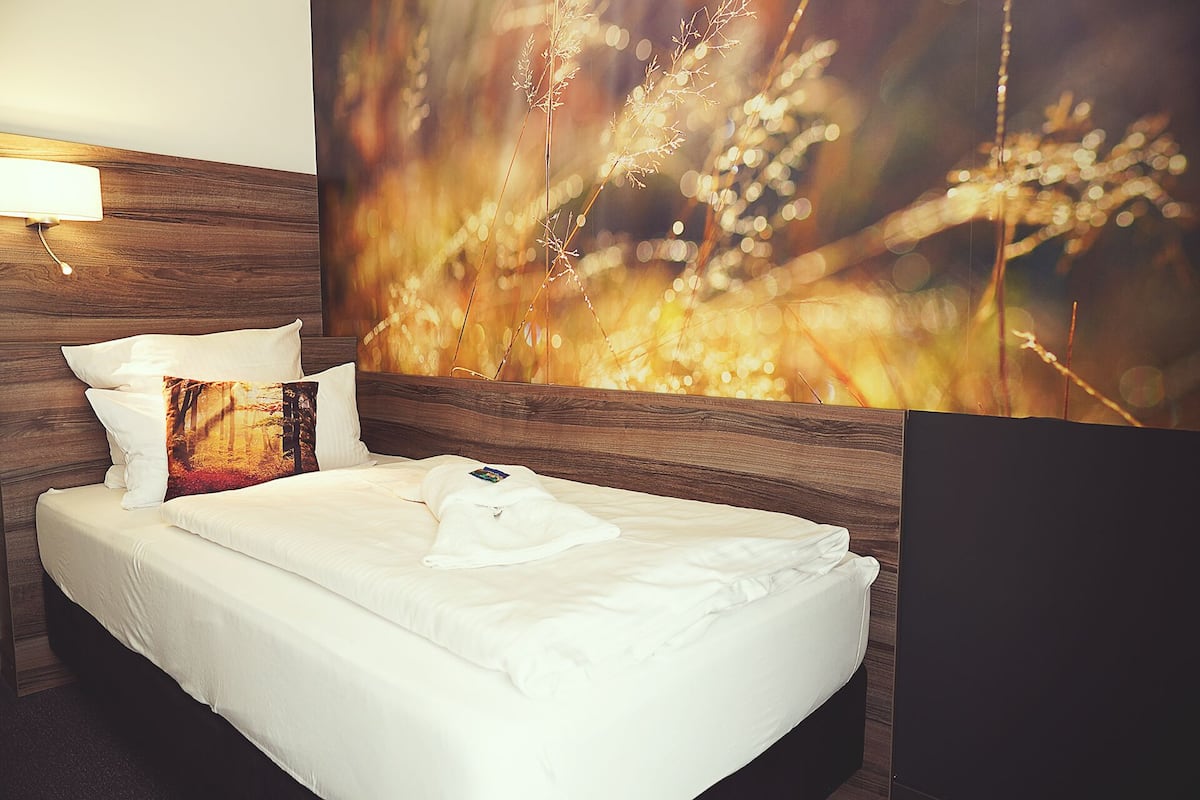 A neatly made bed with white linens and pillows, a wooden headboard, and a large abstract painting on the wall.