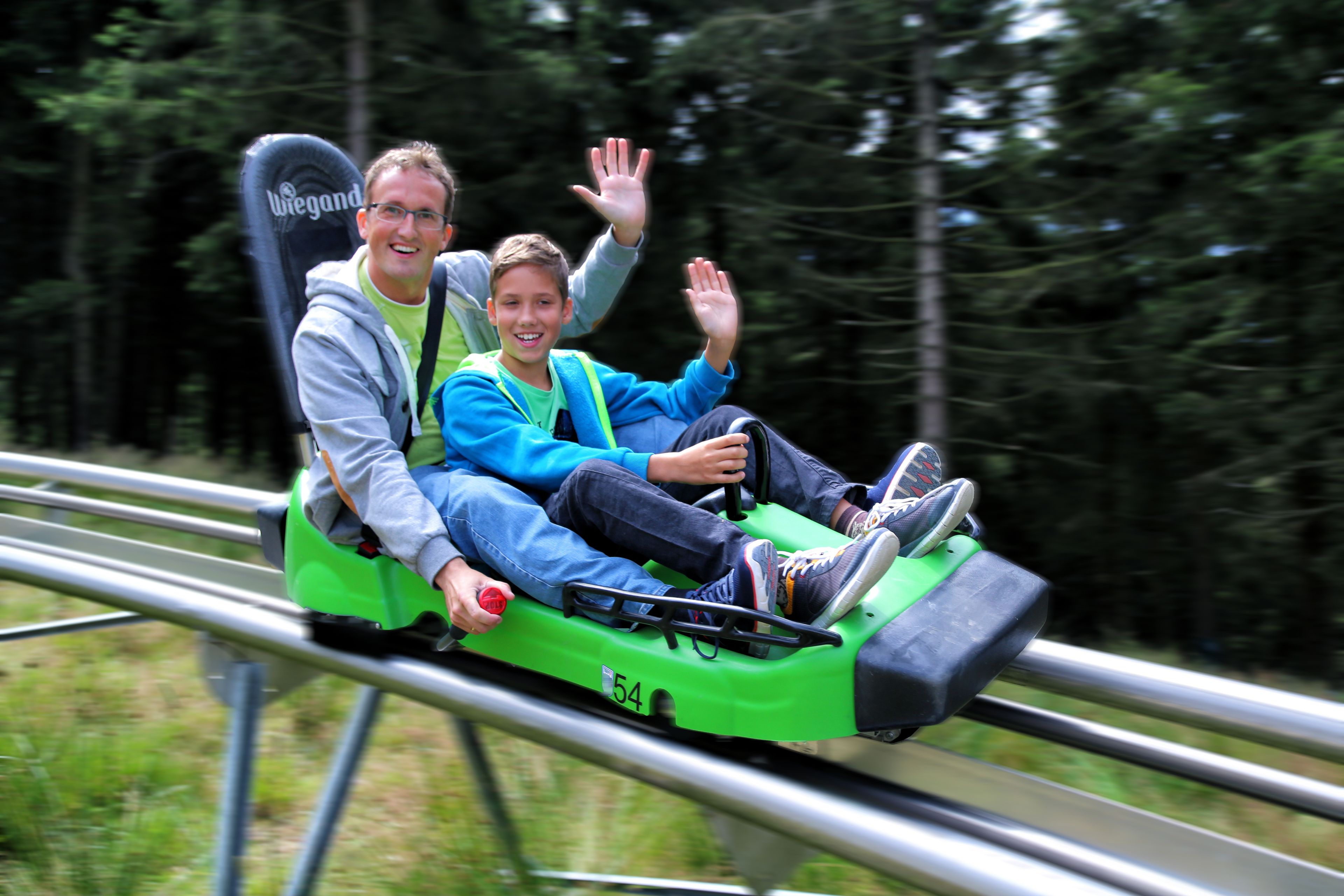 Two people on a green roller coaster with a number 54 on it.