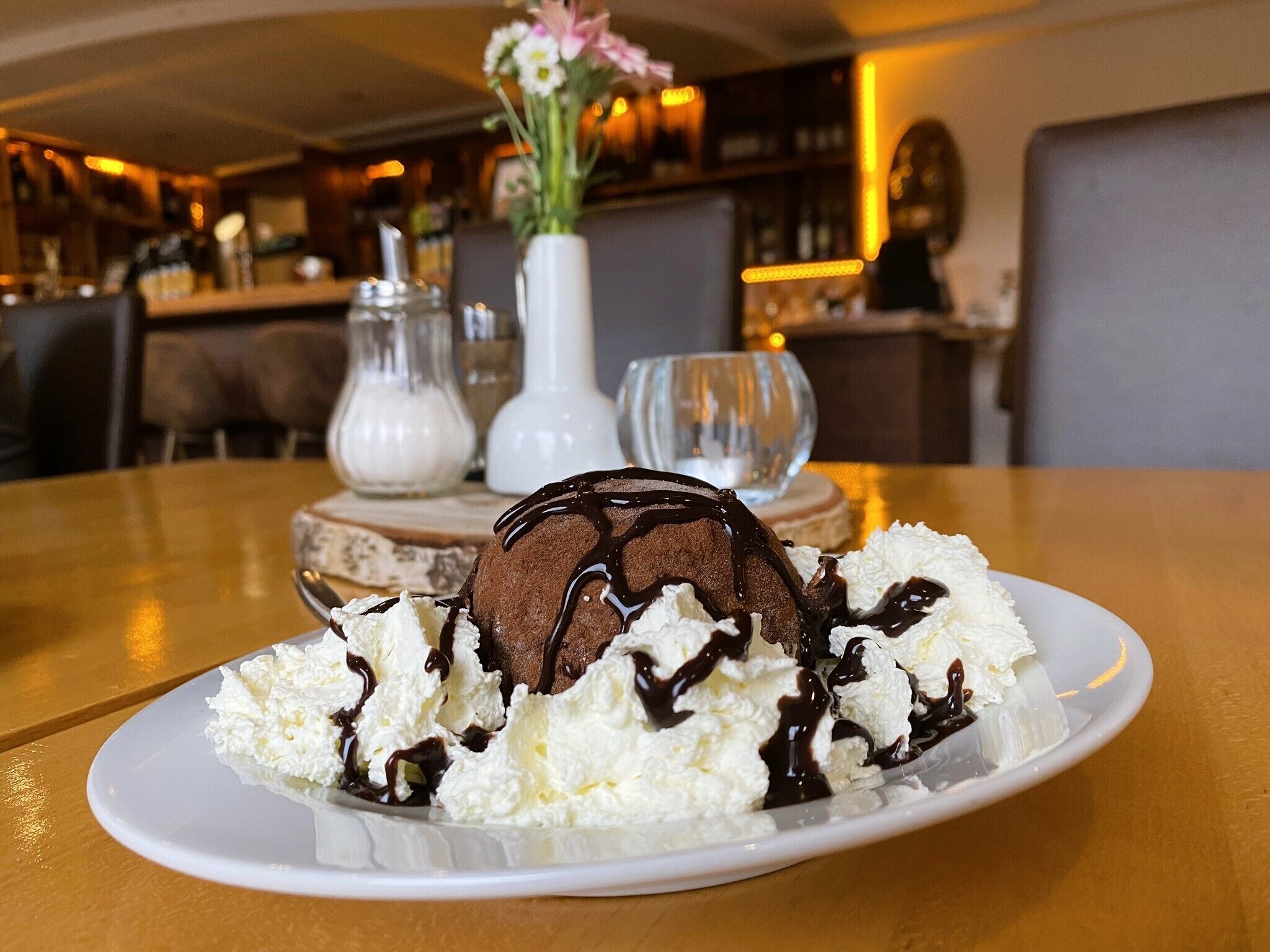 A dessert plate with chocolate ice cream and whipped cream, set on a table in a restaurant.