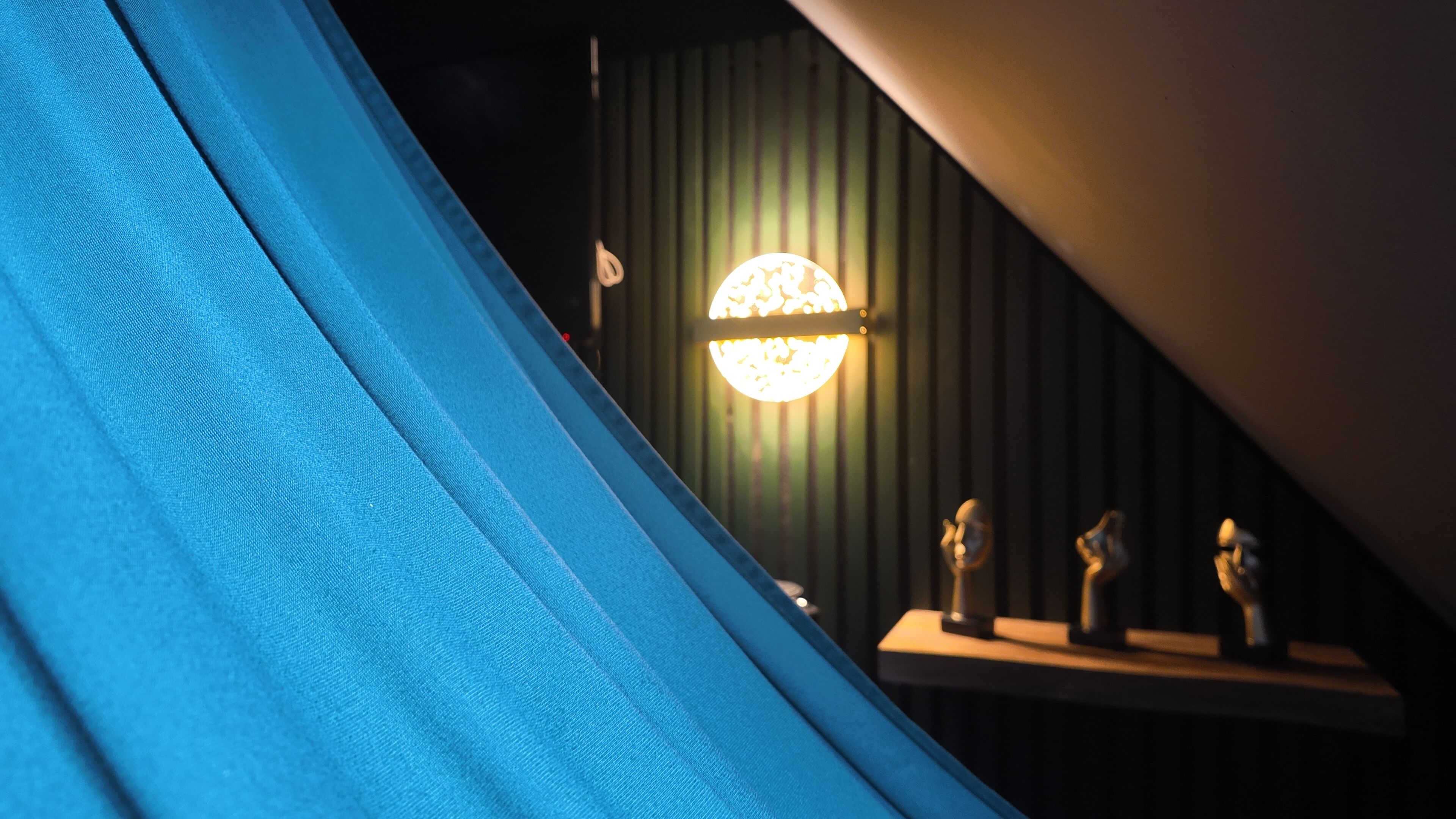 A tent-like structure with a blue fabric, a wall-mounted spherical light fixture, and a small table with three figurines.