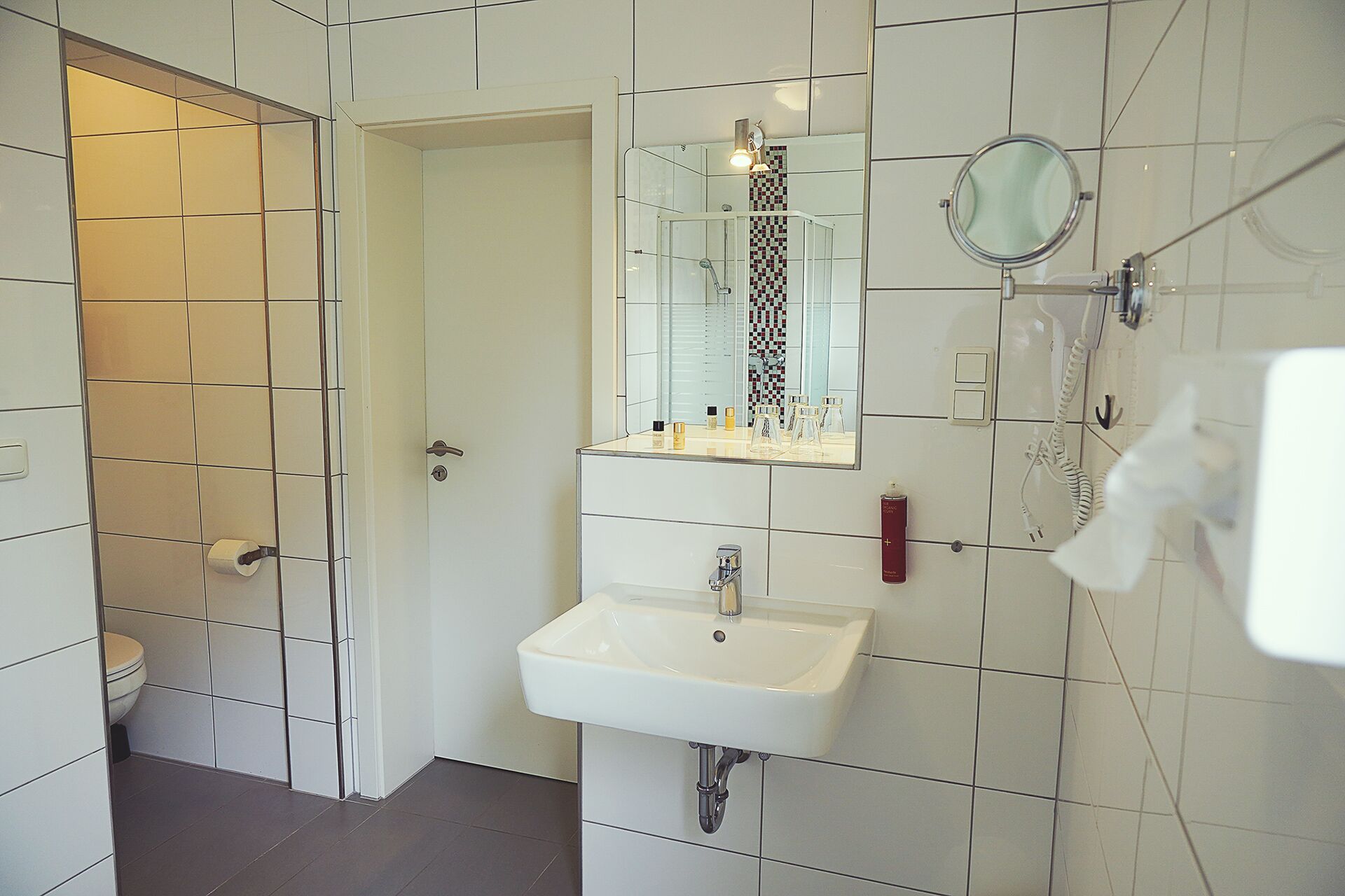 A modern bathroom with a white sink, a glass shower enclosure, a mirror, and a toilet.