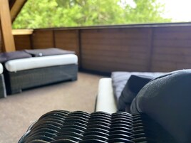 A wicker sofa and a bed with a white mattress in a room with a view of greenery.
