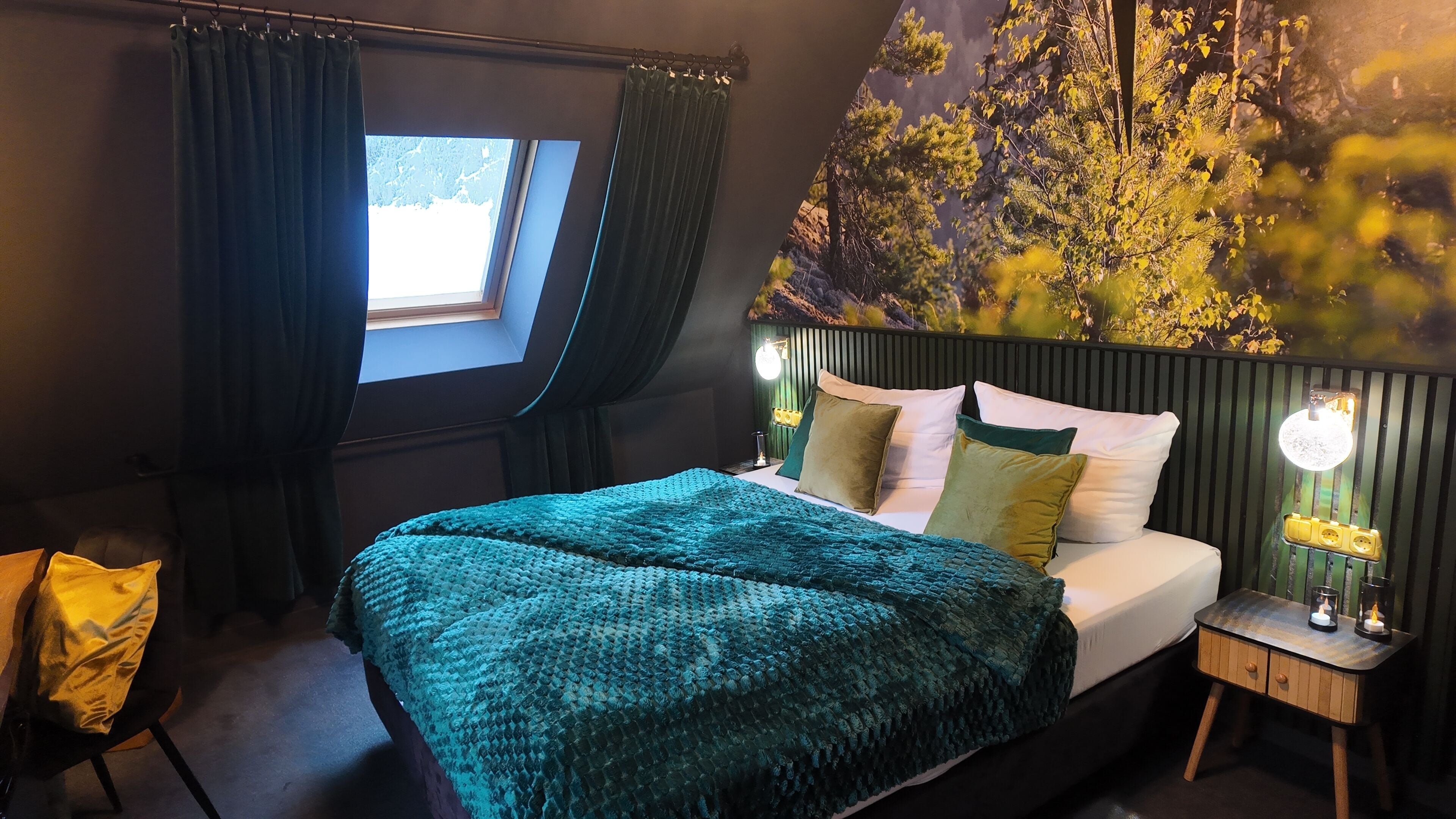 A bedroom with a large bed, a window with curtains, a nightstand with a lamp, and a wall mural.