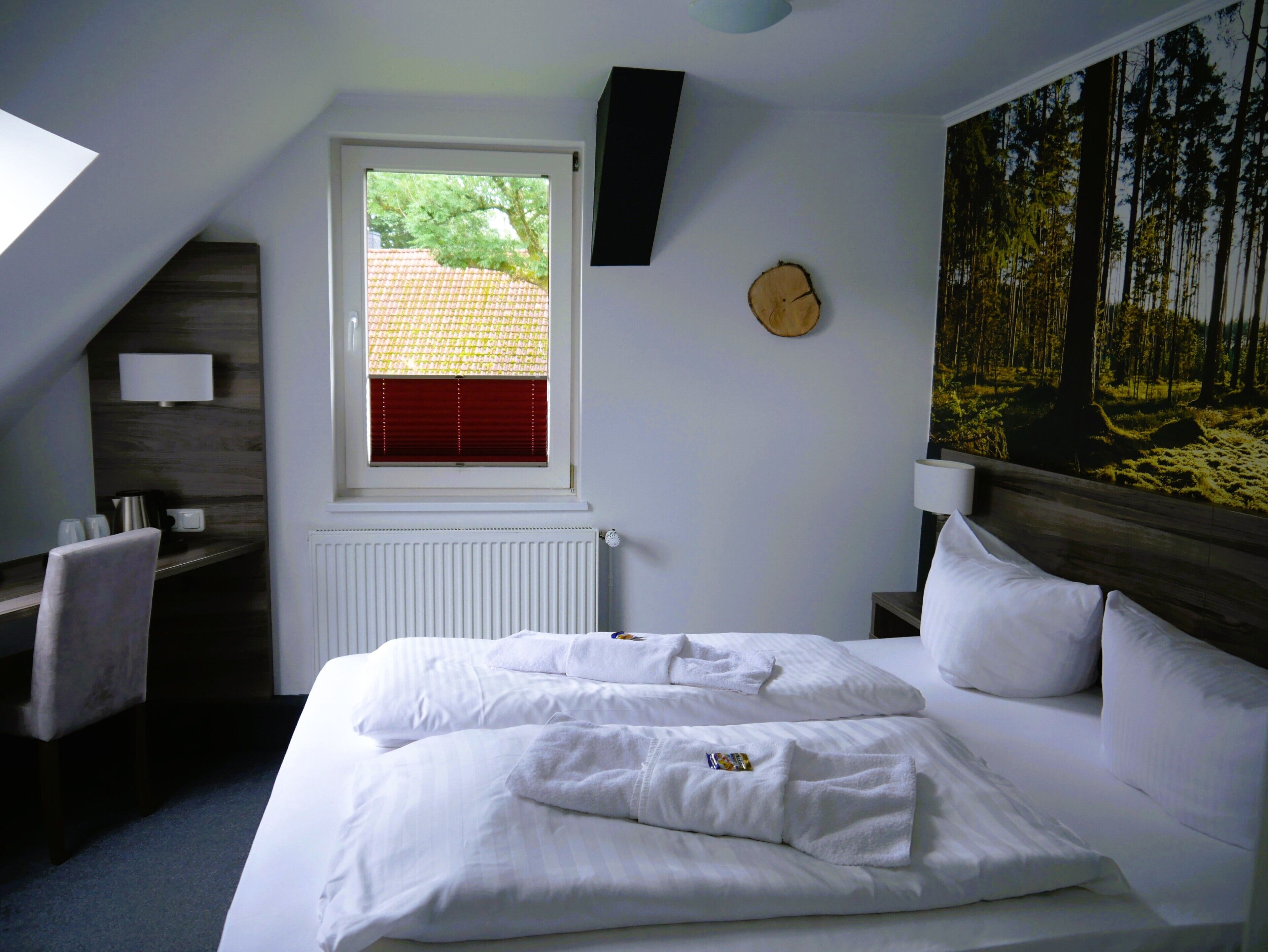 A bedroom with a bed, a desk, a chair, a window with blinds, a radiator, and a wall-mounted clock.