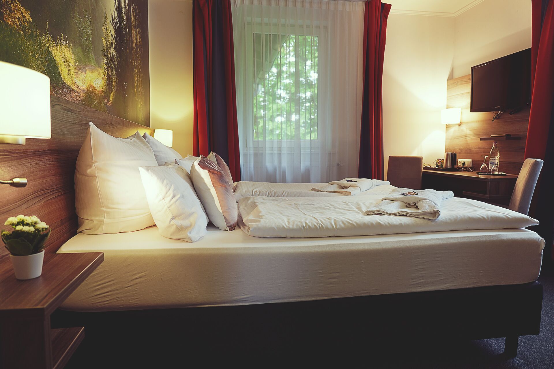 Habitación de hotel con una cama grande, un escritorio, una silla, un televisor y una ventana con cortinas.
