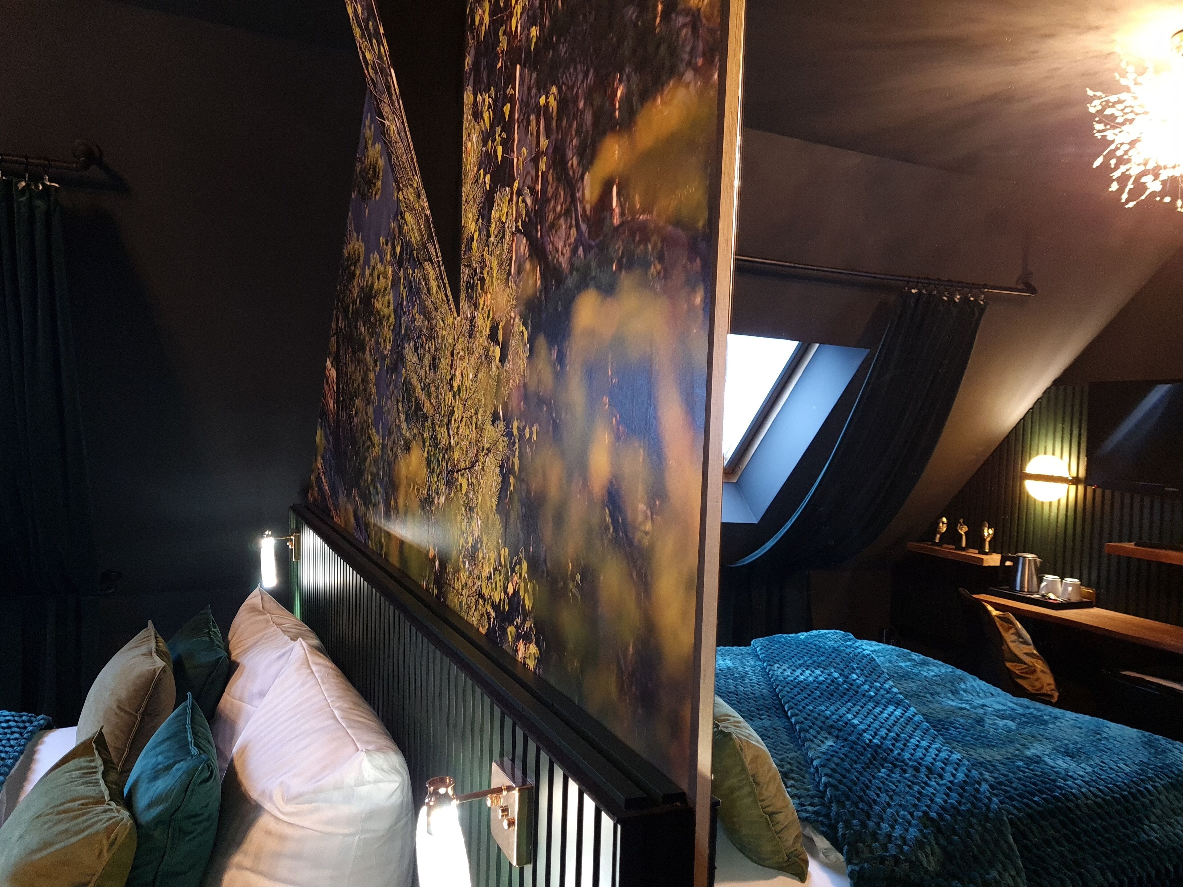 Une chambre avec une grande fenêtre, un lit avec de nombreux oreillers, une table de chevet et un luminaire fixé au mur.