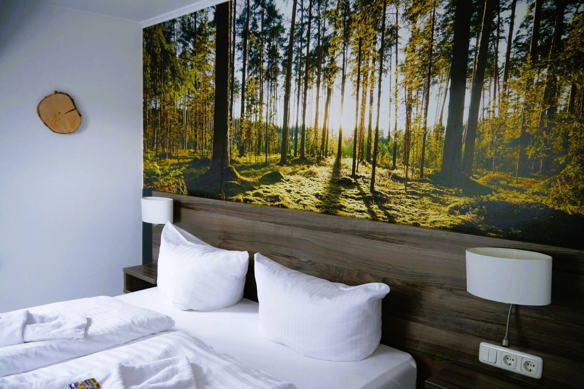 A neatly made bed with white linens and pillows, a wooden headboard, and a wall-mounted lamp.