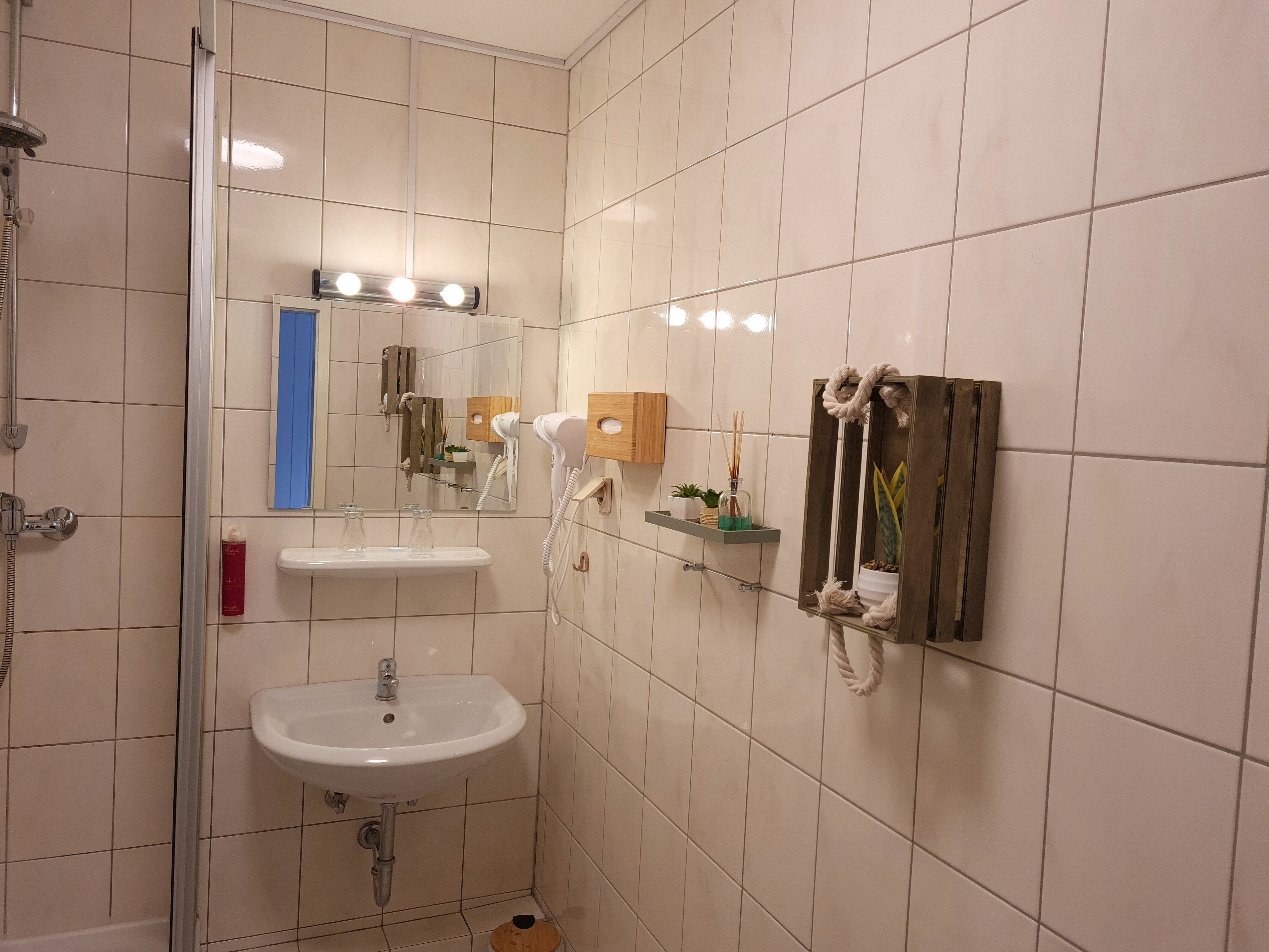 Un baño con lavamanos blanco, espejo, secador de pelo y ducha.