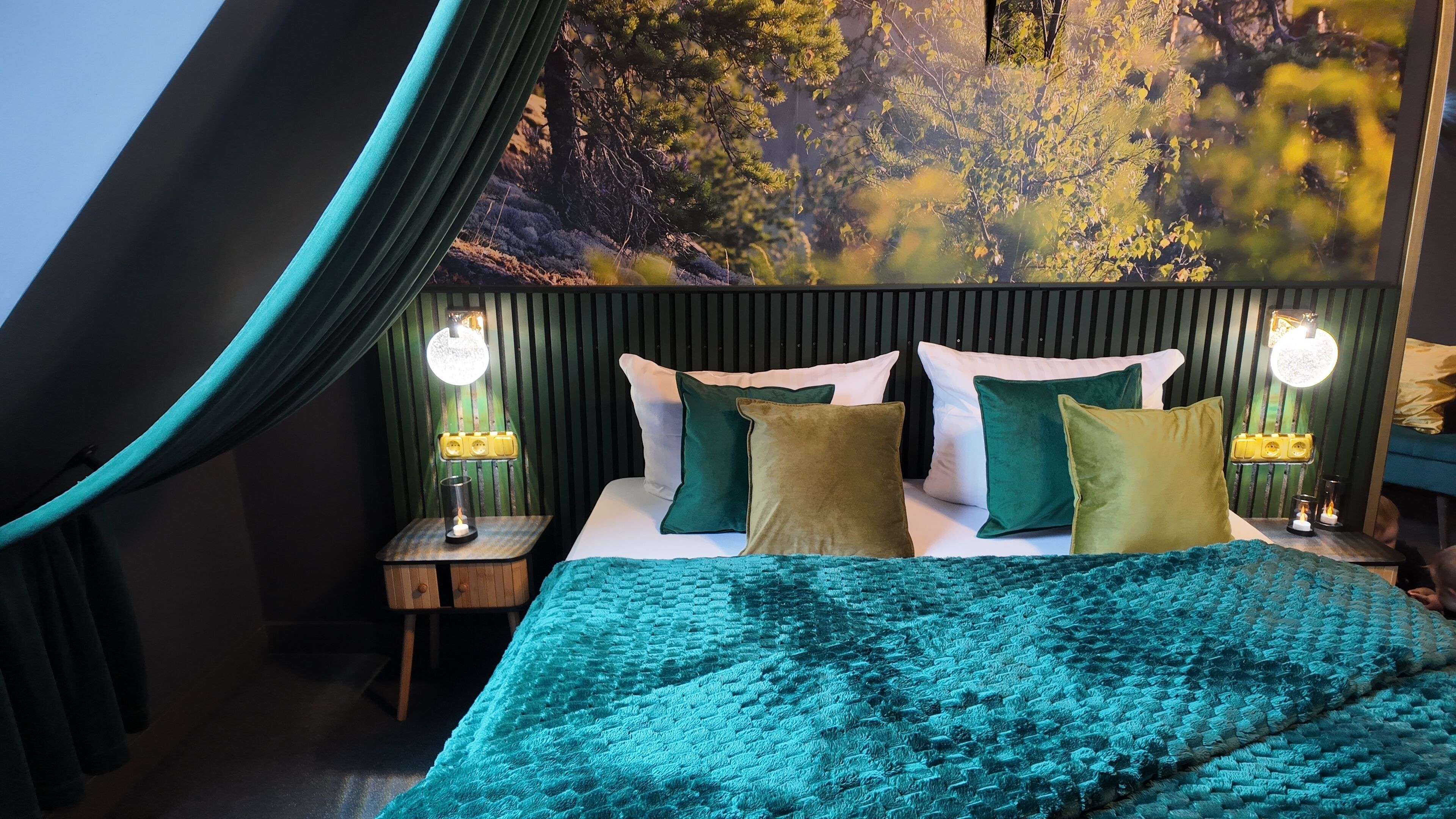 A bedroom with a bed, curtains, a nightstand, and a wall mural.