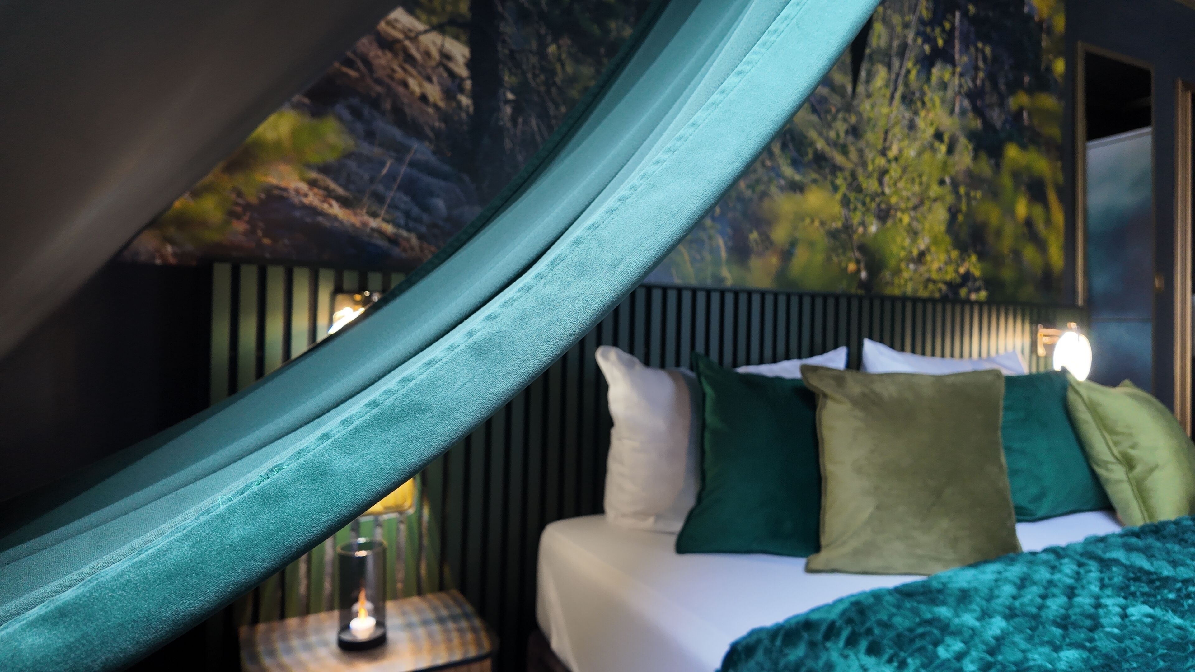 Quarto com cama, almofadas, mesa de cabeceira e luminária na parede.